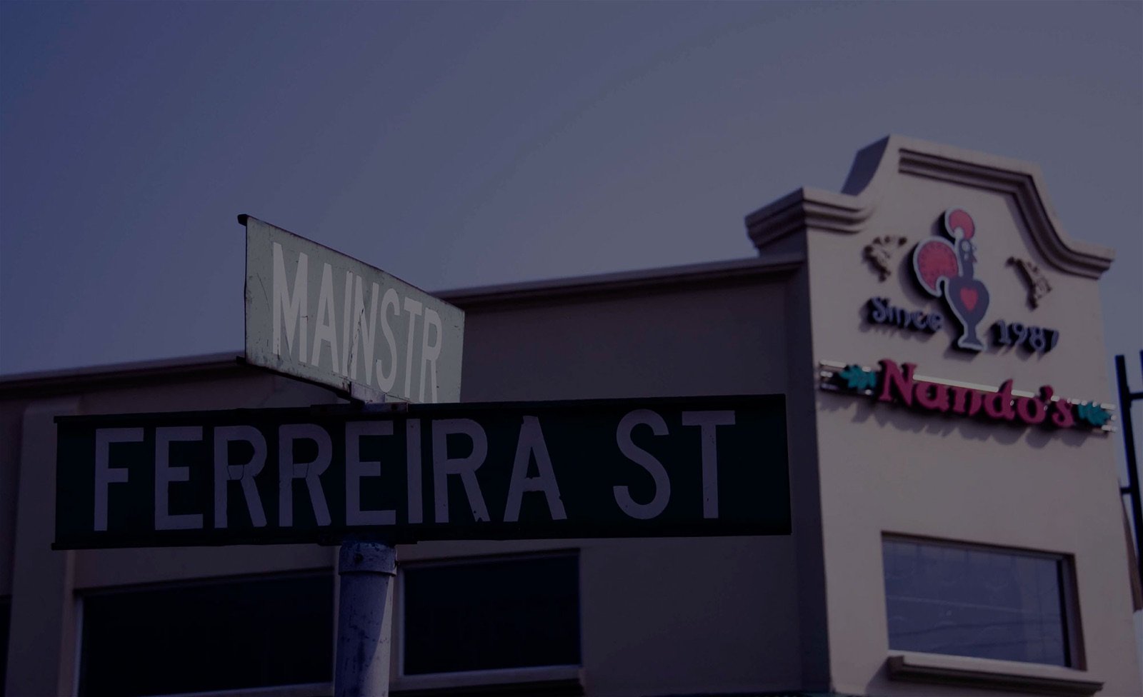 A Ferreira Street sign with a Nando's restaurant in the background